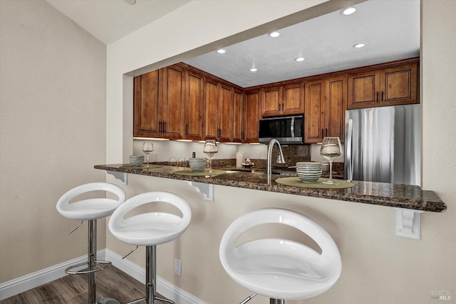 kitchen with dark stone countertops, a breakfast bar area, baseboards, stainless steel appliances, and dark wood-type flooring