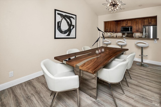 dining room with light wood finished floors, a chandelier, baseboards, and vaulted ceiling