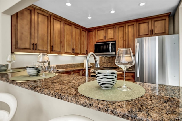 kitchen featuring brown cabinetry, recessed lighting, appliances with stainless steel finishes, and dark stone counters