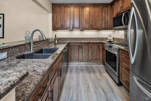 kitchen featuring a sink, dark stone counters, light wood-type flooring, and appliances with stainless steel finishes