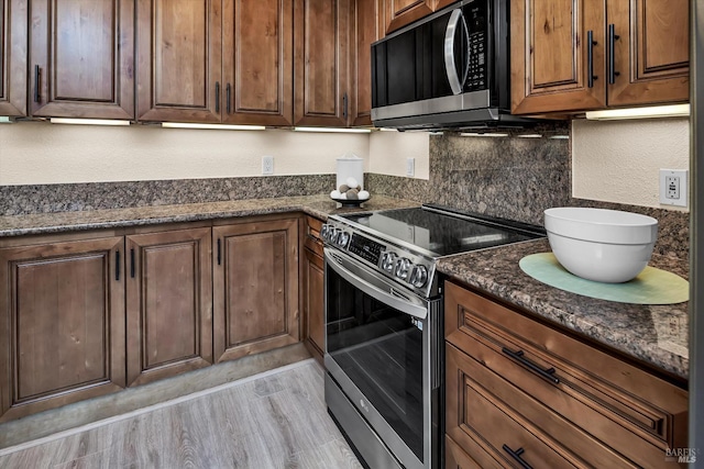 kitchen featuring dark stone counters, light wood finished floors, tasteful backsplash, and appliances with stainless steel finishes