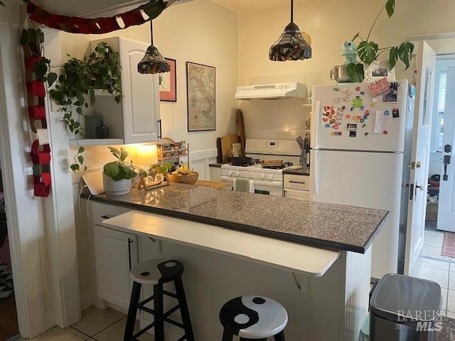 505 Petaluma Blvd N, Petaluma, CA 94952 - kitchen with white appliances, under cabinet range hood, light tile patterned flooring, a breakfast bar area, and dark countertops