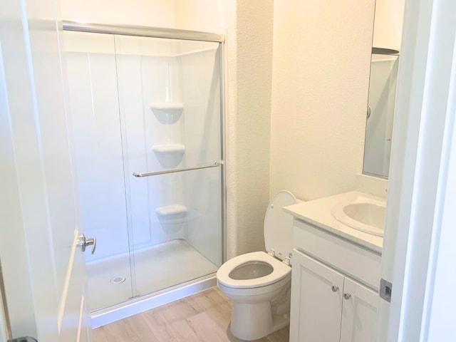 bathroom featuring vanity, wood finished floors, a shower stall, and toilet