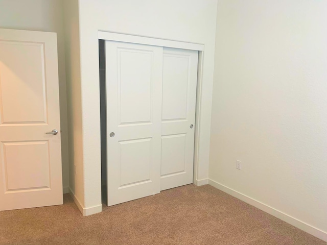 unfurnished bedroom with baseboards, a closet, and light carpet