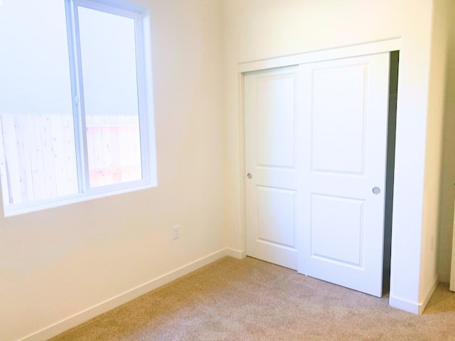 unfurnished bedroom featuring a closet, light colored carpet, and baseboards