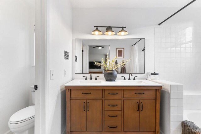 full bathroom with tiled bath, toilet, double vanity, and a sink