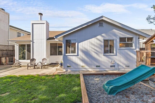 back of house featuring a patio, a lawn, a playground, a chimney, and fence