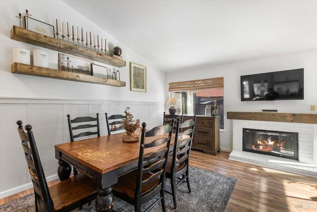 dining area featuring a brick fireplace, a wainscoted wall, lofted ceiling, and wood finished floors