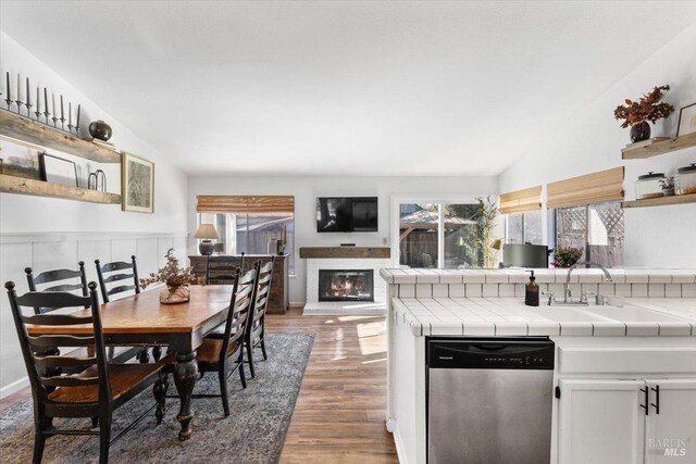 kitchen featuring open shelves, vaulted ceiling, dishwasher, a sink, and tile countertops