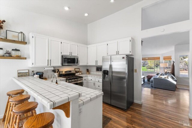 kitchen with white cabinets, appliances with stainless steel finishes, tile countertops, a towering ceiling, and a peninsula