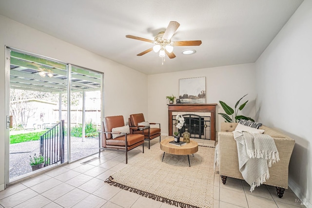 living area featuring a tiled fireplace, light tile patterned floors, a ceiling fan, and visible vents