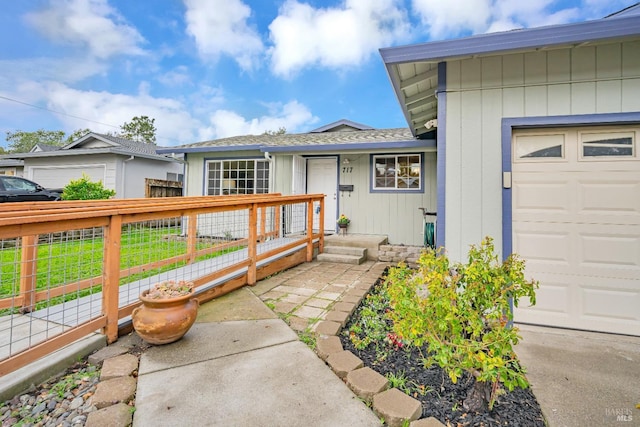 property entrance featuring roof with shingles, a garage, and fence