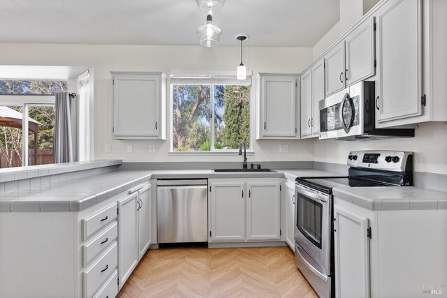 kitchen featuring a sink, stainless steel appliances, a peninsula, and tile counters