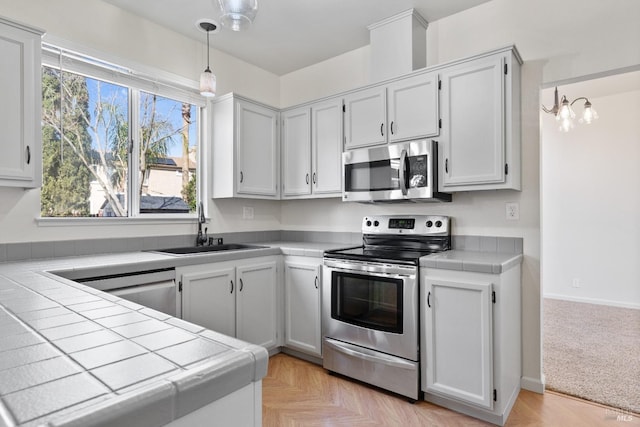 kitchen with decorative light fixtures, a sink, tile countertops, appliances with stainless steel finishes, and baseboards