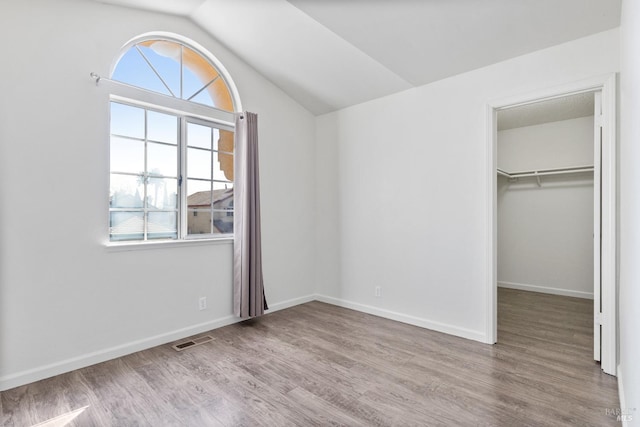 unfurnished bedroom with wood finished floors, visible vents, baseboards, lofted ceiling, and a spacious closet