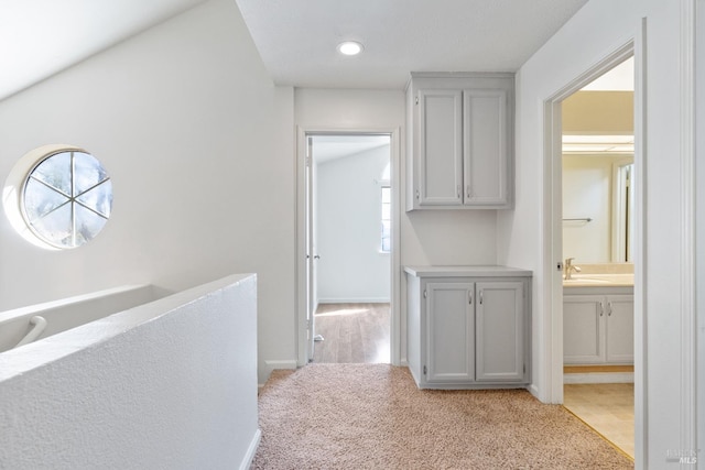 hallway featuring a sink, baseboards, and light carpet