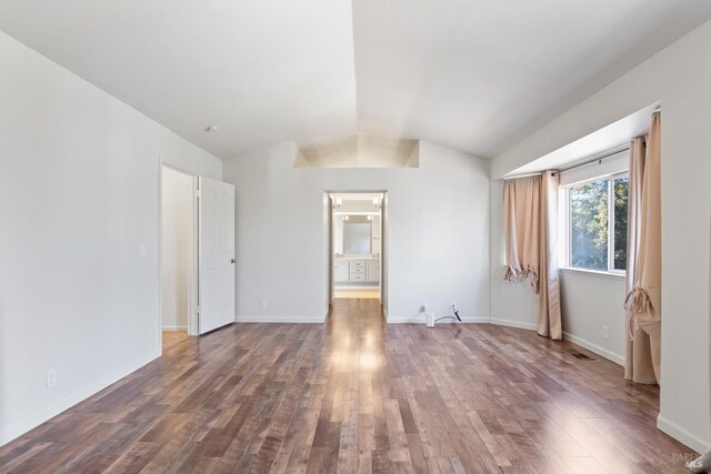 empty room with baseboards, lofted ceiling, and wood finished floors