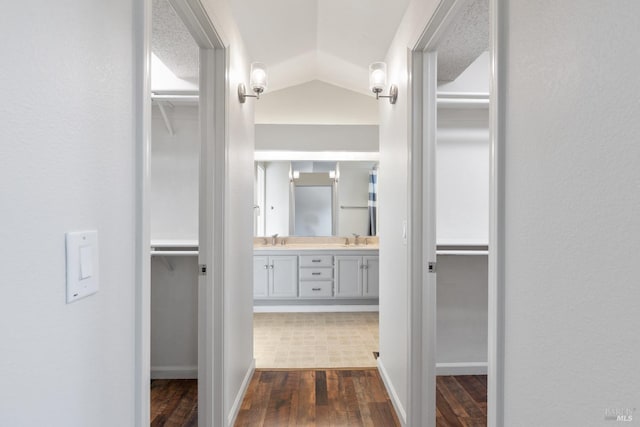 corridor featuring dark wood finished floors, lofted ceiling, and a sink