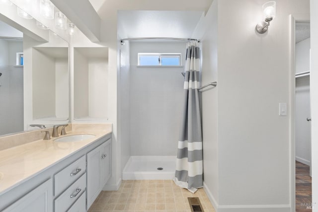 full bath with visible vents, baseboards, vanity, and a tile shower