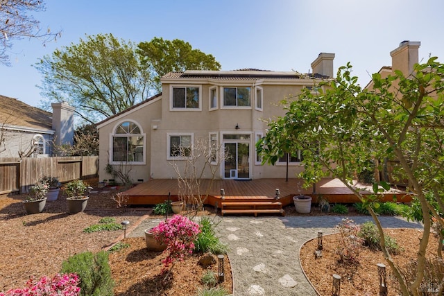 back of house featuring stucco siding, roof mounted solar panels, a deck, and fence