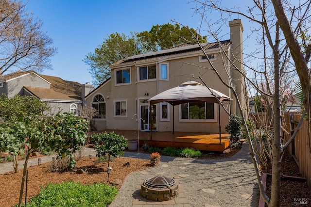 rear view of house with stucco siding, fence, an outdoor fire pit, a wooden deck, and solar panels