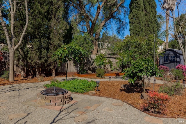 view of yard featuring fence, an outdoor structure, a storage unit, a fire pit, and a patio area