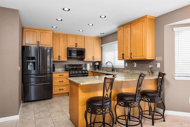 kitchen featuring a kitchen bar, recessed lighting, appliances with stainless steel finishes, a peninsula, and light stone countertops