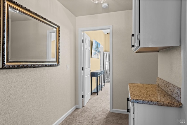 hall featuring baseboards, carpet flooring, and a textured wall