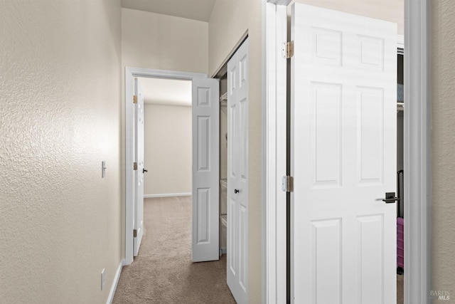 hallway featuring a textured wall, dark colored carpet, and baseboards