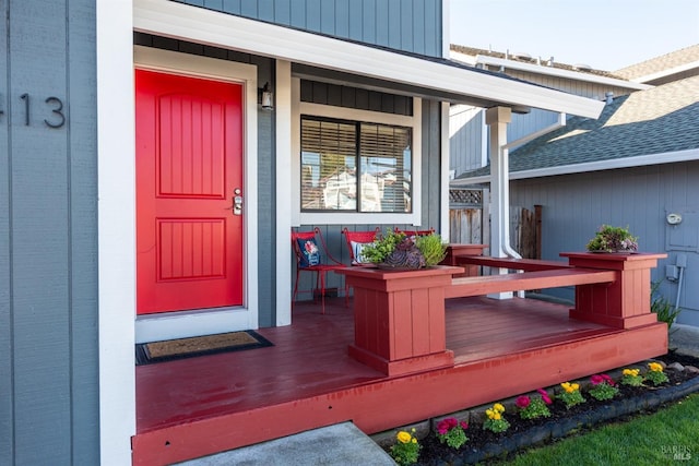 view of exterior entry with covered porch and roof with shingles