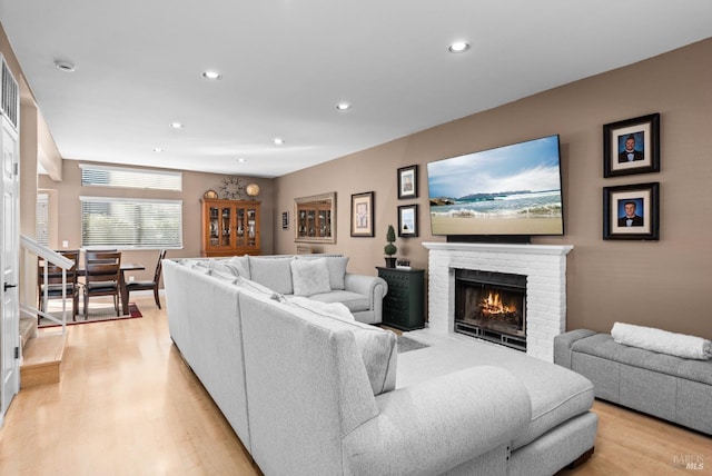 living area featuring recessed lighting, light wood-style flooring, a brick fireplace, and stairs