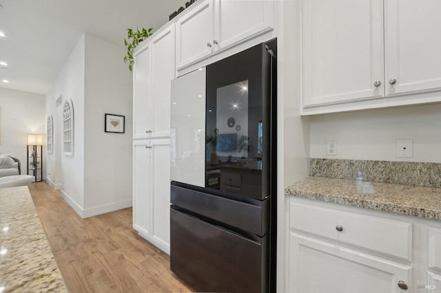 kitchen with light wood-type flooring, baseboards, white cabinets, refrigerator with glass door, and light stone countertops