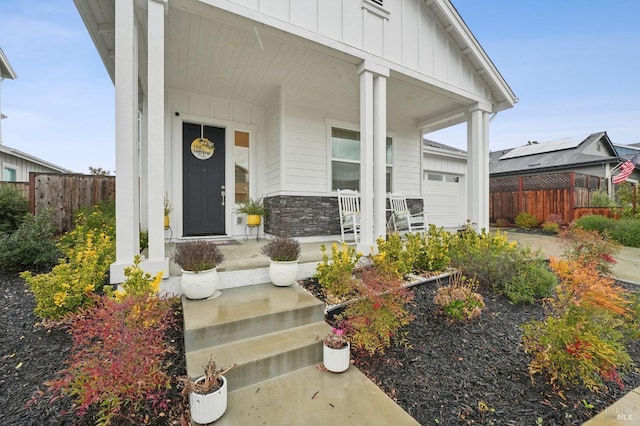 view of exterior entry with board and batten siding, fence, a porch, a garage, and stone siding