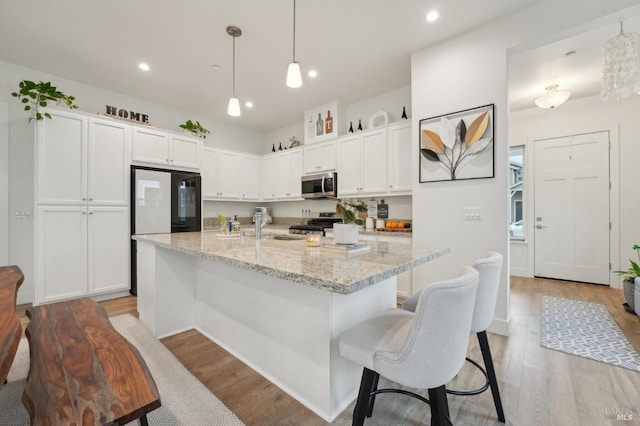 kitchen featuring stainless steel microwave, white cabinets, light wood-style floors, and a sink