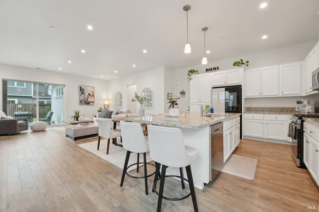 kitchen featuring light stone countertops, open floor plan, appliances with stainless steel finishes, and light wood-type flooring