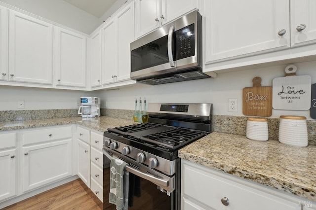 kitchen with light stone counters, light wood-style floors, appliances with stainless steel finishes, and white cabinetry