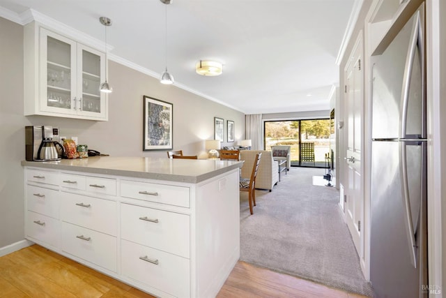 kitchen featuring ornamental molding, freestanding refrigerator, a peninsula, light countertops, and glass insert cabinets