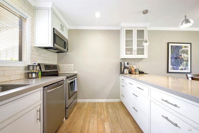 kitchen featuring light wood finished floors, glass insert cabinets, crown molding, decorative backsplash, and appliances with stainless steel finishes