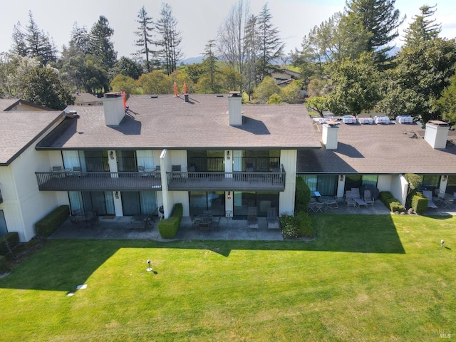 rear view of house with a patio, a balcony, a chimney, and a lawn