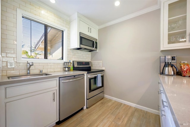 kitchen featuring a sink, backsplash, stainless steel appliances, light wood-style floors, and crown molding