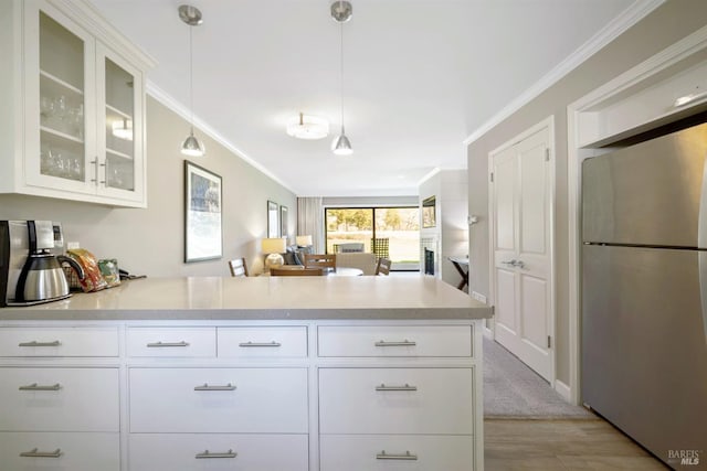 kitchen with a peninsula, light countertops, freestanding refrigerator, and ornamental molding