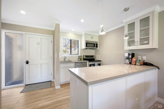 kitchen with a sink, appliances with stainless steel finishes, a peninsula, crown molding, and glass insert cabinets