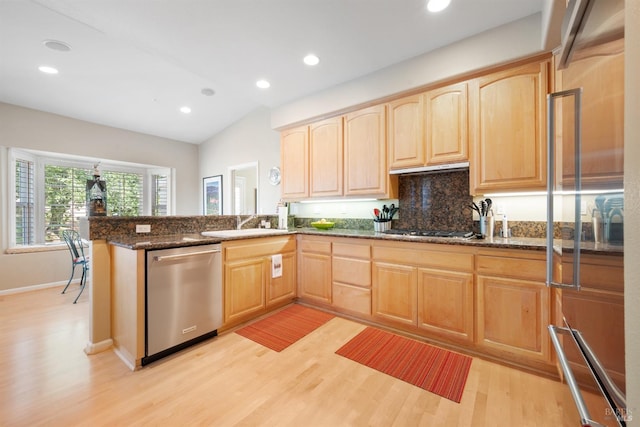 kitchen featuring light brown cabinets, dark stone counters, a peninsula, light wood-style floors, and stainless steel appliances