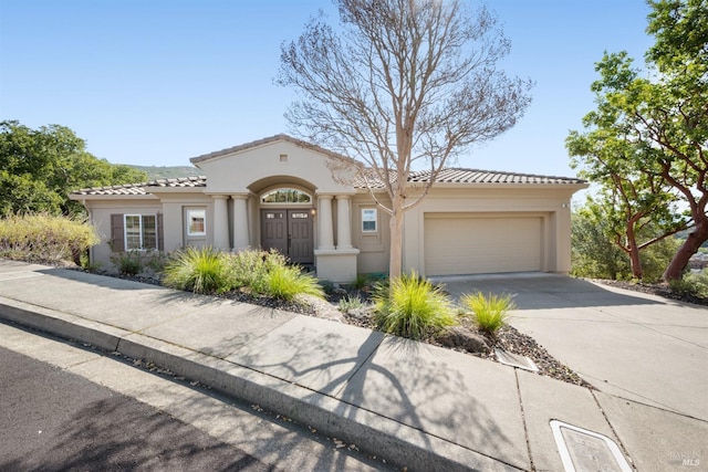 mediterranean / spanish house with stucco siding, concrete driveway, an attached garage, and a tile roof