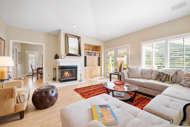 living room featuring built in shelves, wood finished floors, recessed lighting, french doors, and a glass covered fireplace