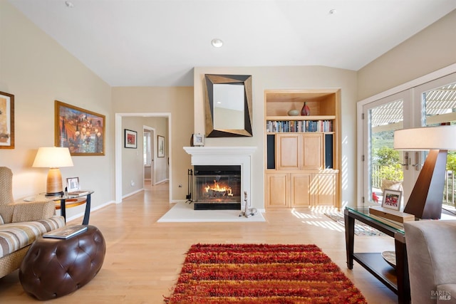 living area featuring built in shelves, baseboards, wood finished floors, and a glass covered fireplace