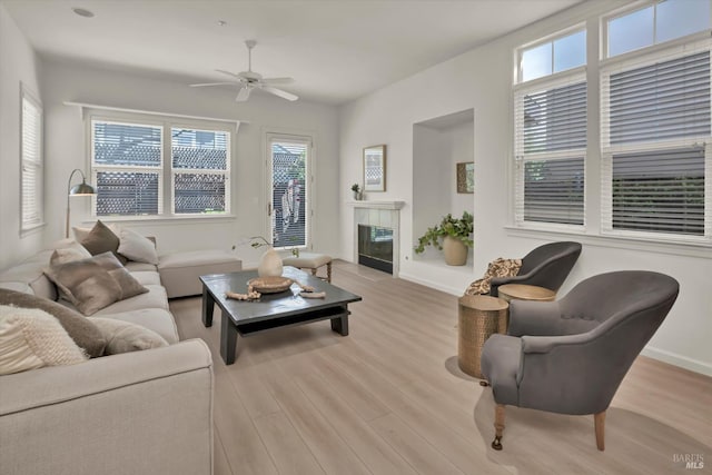 living area featuring baseboards, a fireplace with flush hearth, wood finished floors, and a ceiling fan