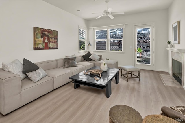 living room with a high end fireplace, a ceiling fan, and light wood-style floors