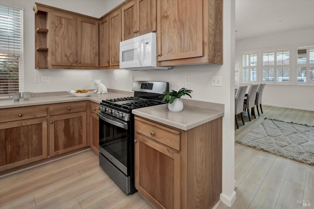 kitchen featuring white microwave, open shelves, light wood-style flooring, light countertops, and gas range