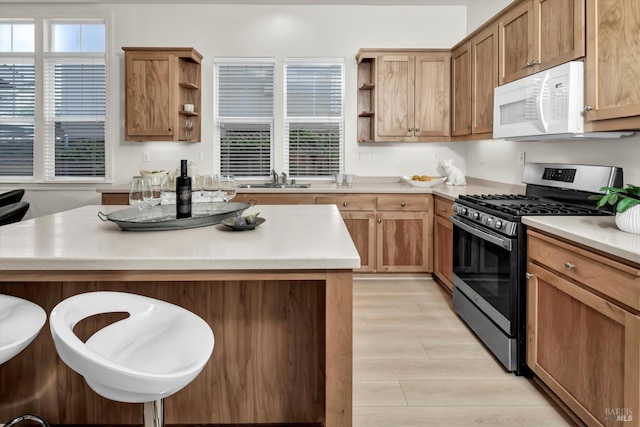 kitchen with white microwave, open shelves, stainless steel range with gas stovetop, a kitchen bar, and a sink